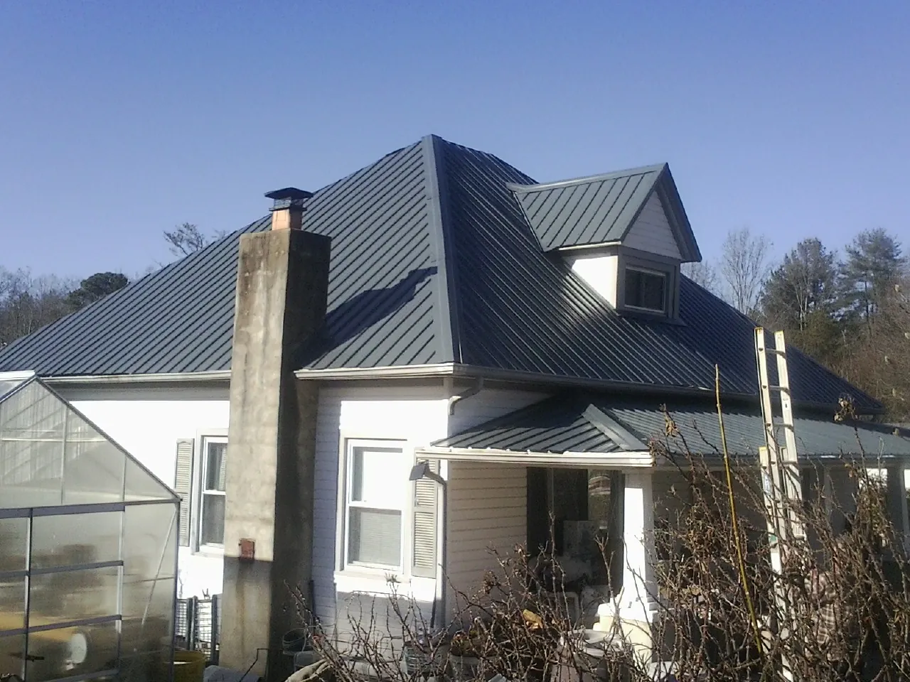 Dark blue standing seam metal roof on a white farmhouse with dormer — Slate & Tile Roof Repair by Roofing Brothers in Corning