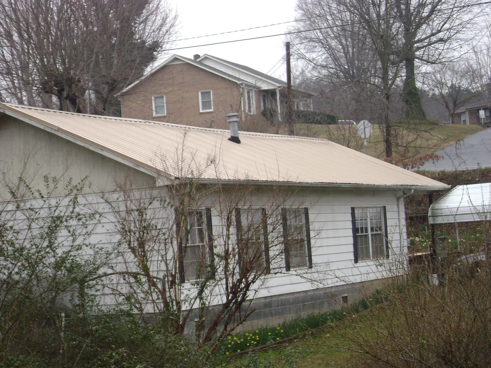Tan metal roof on a white sided house set into a hillside — Commercial Roofing by Roofing Brothers in Corning