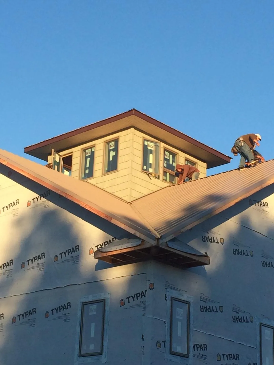 Roofers working around a rooftop cupola on a new metal roof at sunset — Roof Waterproofing in Corning by Roofing Brothers